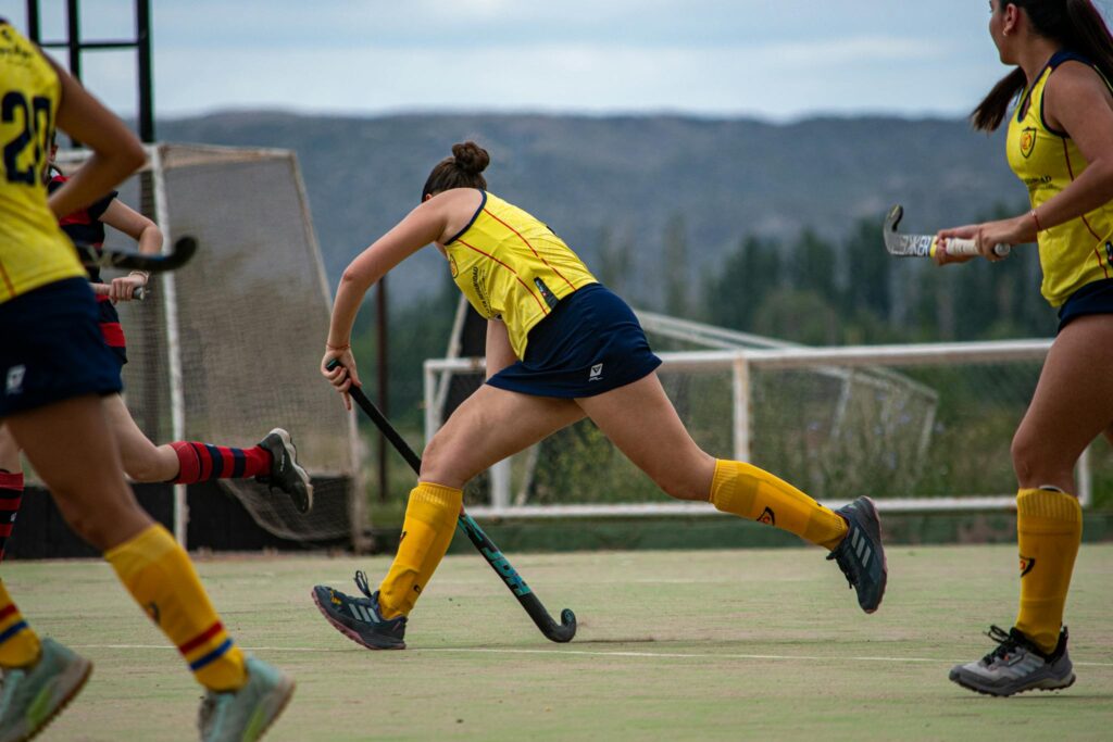 Action shot of a women's field hockey match outdoors, showcasing athleticism and teamwork.