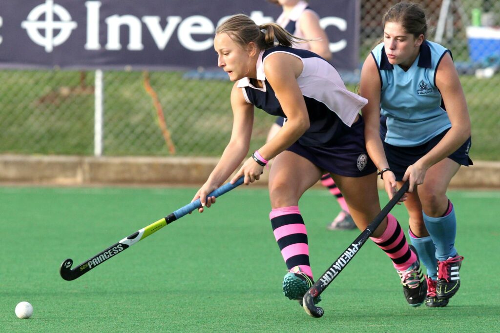 Dynamic action shot of women playing field hockey during a competitive match on a grass field.